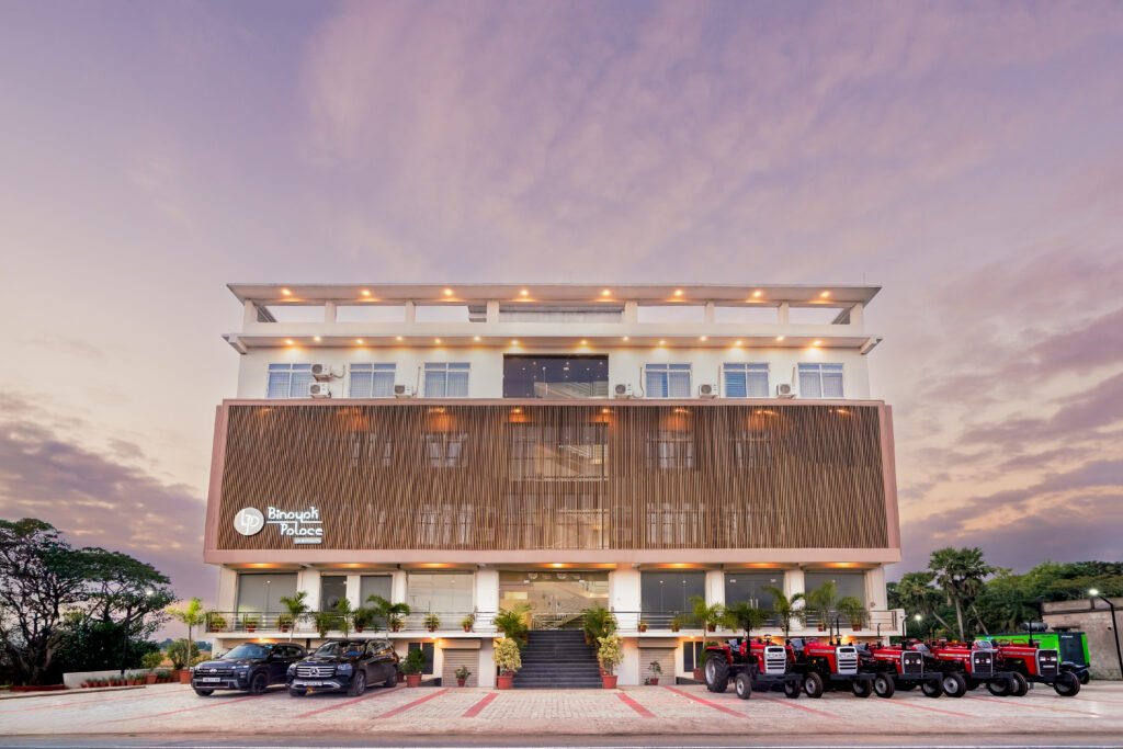 Elegant multi-story hotel building in Kendrapara with modern architecture, luxury vehicles, and tractors parked in front.